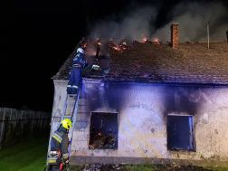 Füstölgő ház a háttérben, tűzoltók oltják